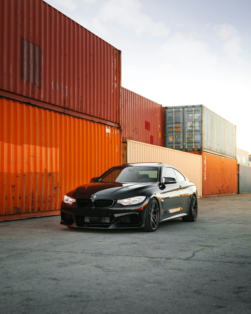 Black sports car parked near shipping containers, ready for international car transport.