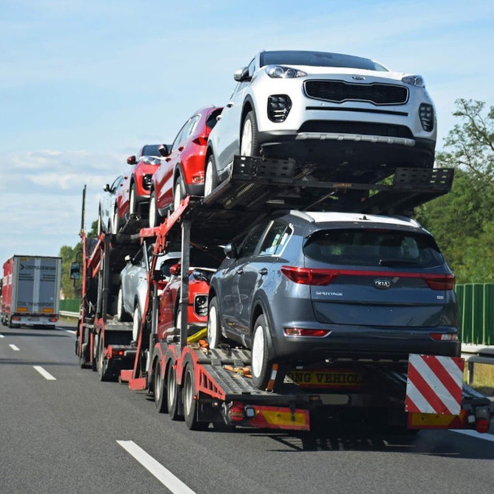 Car shipping truck transporting multiple vehicles on highway under a clear blue sky.