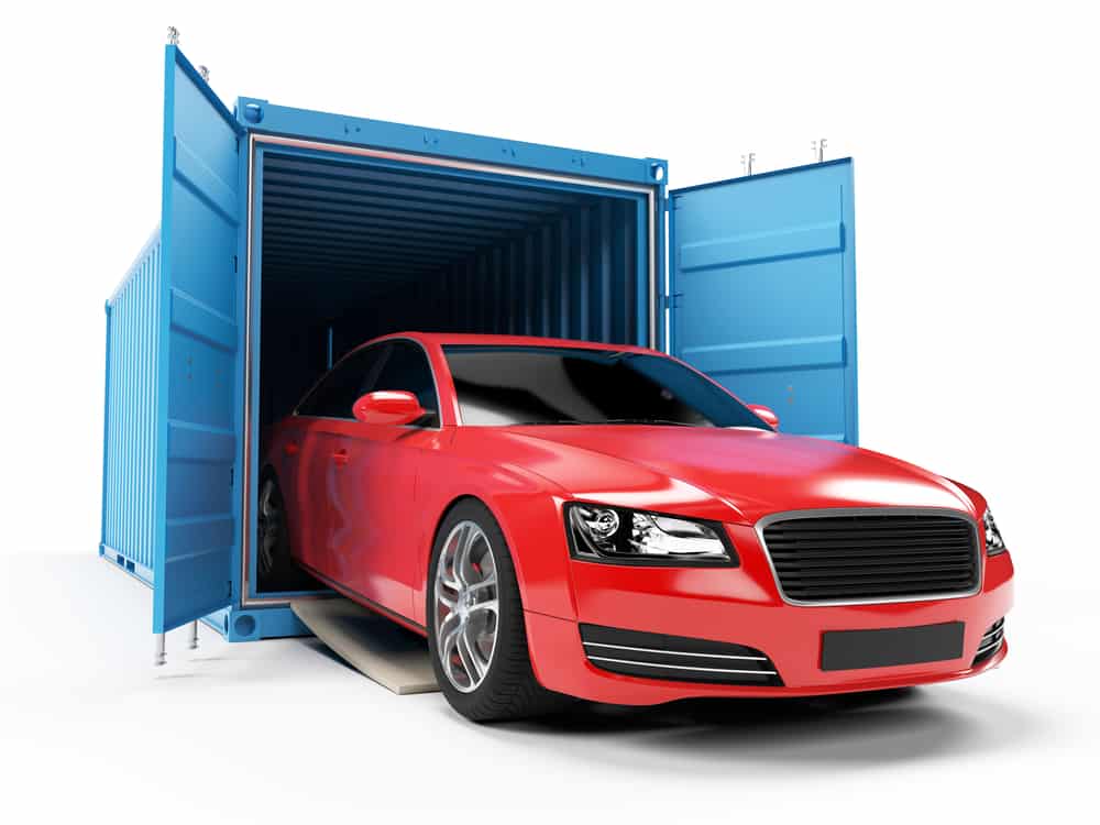 Bright red car emerges from open blue shipping container, ready for delivery or transport.