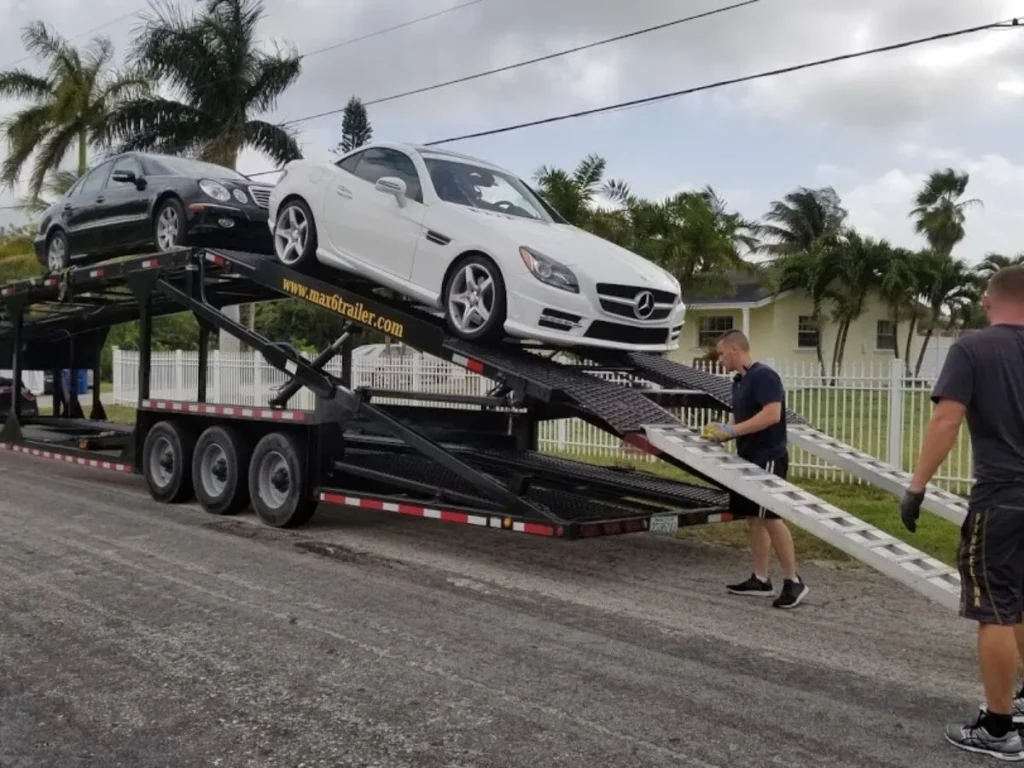 Workers loading cars onto an open car carrier trailer for transport and shipping.