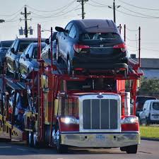 Car carrier truck transporting multiple vehicles for shipping on an open trailer along a roadway.