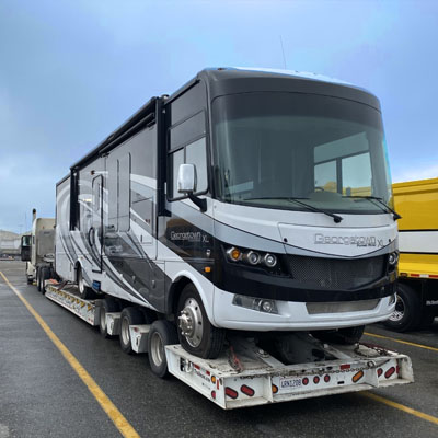 A large RV motorhome being transported on a heavy-duty flatbed trailer at a parking area.