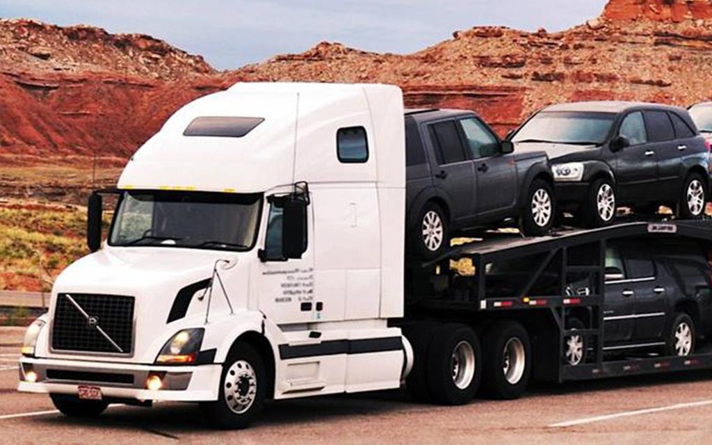 Truck hauling SUVs in desert area, showcasing specialized overseas shipping for vehicles in transit.