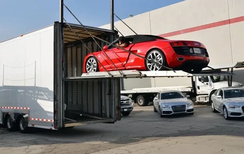 Red sports car loading into enclosed trailer for specialized freight services in the automotive sector.